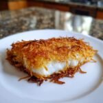 A perfectly cooked fish fillet with an Irresistible Crispy Potato Crusted coating served on a white plate.