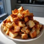 A generous pile of golden brown, Crunchy Homemade Croutons stacked high on a white plate.