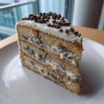 A tall slice of Delicious Cannoli Layer Cake Recipe showing three layers of cake, creamy filling with chocolate chips, and mini chocolate chips on top.