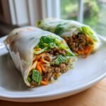 Two Delicious Lemongrass Beef Spring Rolls filled with seasoned ground beef, carrots, and mint on a white plate.