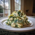 A mound of Delicious Spinach Artichoke Chicken Salad featuring chunks of chicken, spinach, and artichoke hearts in a creamy dressing.