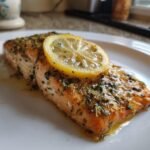 Close-up of a perfectly cooked fillet of Delightful Baked Lemon Herb Salmon topped with herbs and a lemon slice.