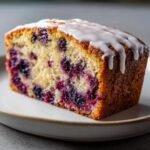Close-up of a moist slice from the Delightful Blackberry Lemon Loaf Recipe, topped with white lemon glaze.