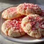 A close-up of several Delightful Easy Peppermint Cookies topped with crushed candy canes on a white plate.