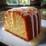 A moist slice of Delightful Lemon Pound Cake topped with thick white lemon glaze and zest.