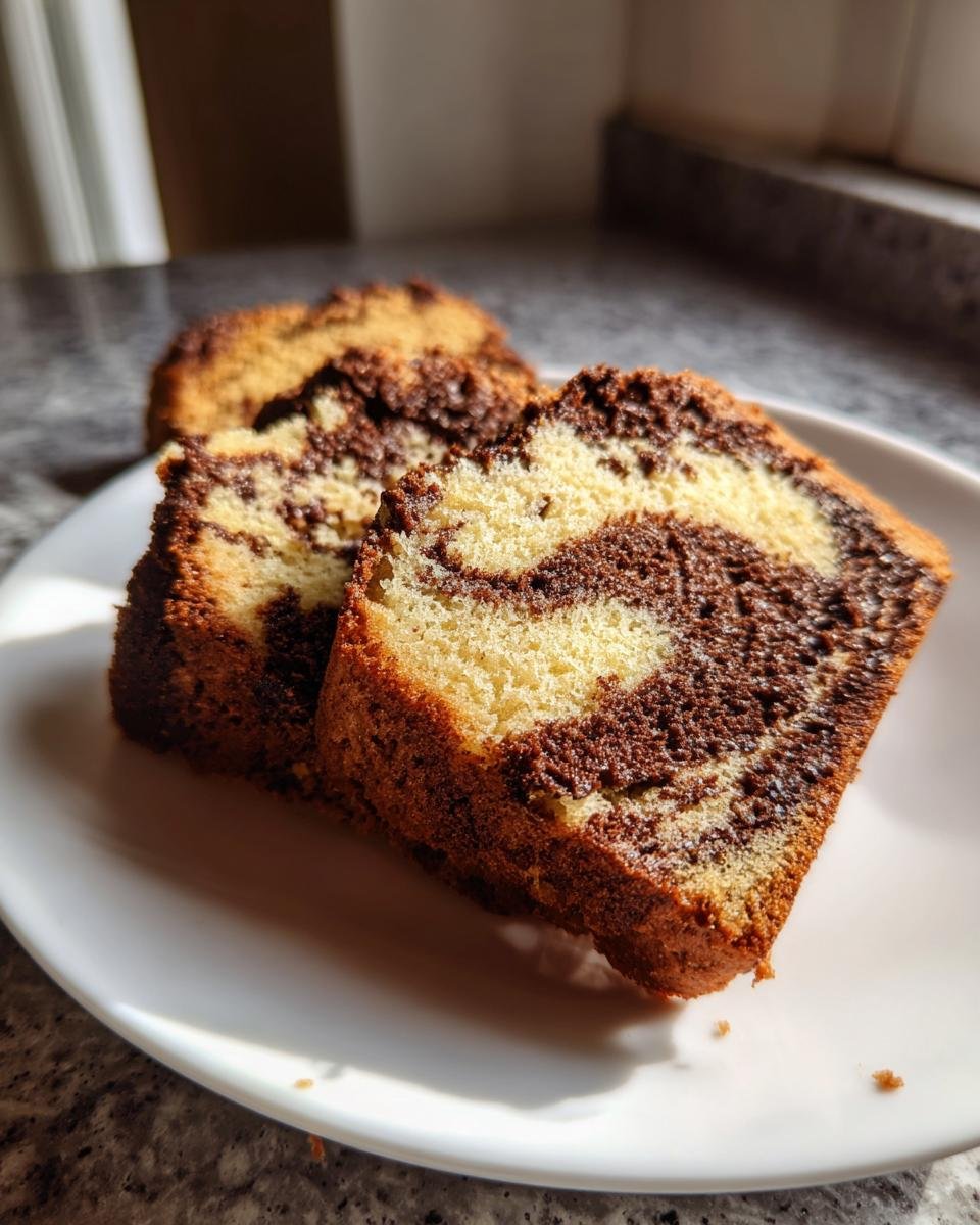 Two moist slices of Easy And Moist Marble Cake showing the distinct vanilla and chocolate swirls on a white plate.