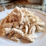Close-up of perfectly seasoned, Easy Crockpot Shredded Chicken piled on a white plate.
