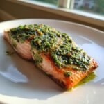 A close-up of a perfectly cooked fillet of Easy Pesto Salmon 3 Ingredients In Just 20 Minutes on a white plate.