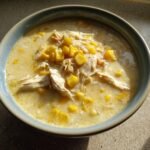 Close-up of a creamy bowl of Fiesta Chicken Corn Chowder topped with shredded chicken and bright yellow corn kernels.