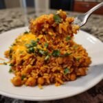 A fork lifts a bite of Flavorful Taco Spiced Chickpea and Rice Skillet, topped with melted cheese and cilantro.