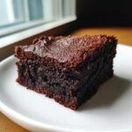 A close-up of a single, dense slice of fudgy espresso brownies on a white plate.