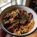 Close-up of Irresistible Garlic Butter Steak Lightning Noodles topped with glossy beef chunks and green onions.