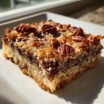 A single serving of rich Grain Free Magic Cookie Bars topped with toasted coconut and whole pecans, sitting on a white plate.