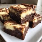 Four squares of Indulgent Cheesecake Brownies Recipe stacked on a white plate, showing rich dark chocolate base and swirled cream cheese topping.