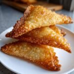 Close-up of three golden-brown, crispy Irresistible Beef Sambusa stacked on a white plate.