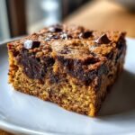 Close-up of a thick, chewy slice of Irresistible Blondies With Chocolate Chips on a white plate.