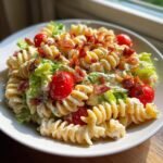 A close-up of Irresistible BLT Pasta Salad featuring rotini pasta, creamy dressing, cherry tomatoes, lettuce, and crispy bacon.