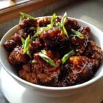 Close-up of bite-sized pieces of Irresistible Bourbon Chicken Sweet Tangy Delight Recipe coated in a glossy dark sauce and garnished with green onions.