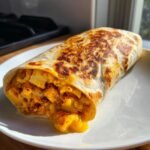 Close-up of an Irresistible Cheesy Potato Burritos, showing a grilled tortilla stuffed with cheesy potatoes oozing out.