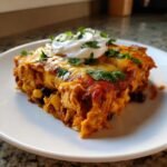 A generous slice of Irresistible Chicken Nacho Casserole topped with melted cheese, sour cream, and cilantro.