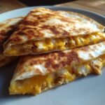 Close-up of golden-brown, toasted Irresistible Chicken Quesadillas cut into wedges, showing melted cheddar and white cheese with shredded chicken.