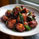 A close-up of glossy, dark brown pieces of Irresistible Chinese Three Cup Chicken topped with fresh basil leaves.