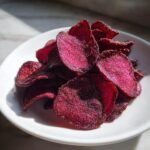 A pile of vibrant, deep magenta Irresistible Crispy Beet Chips seasoned with spices, served in a small white bowl.