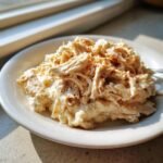 A close-up of shredded, creamy Crockpot Ranch Chicken served on a white plate, sprinkled with paprika.