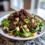 A plate featuring the Irresistible Gingerbread Cookie Crumble Salad with greens, apples, pecans, cranberries, and dark crumble topping.