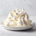 A beautiful mound of fluffy, white Irresistible Homemade Cream Cheese Frosting piled high on a small white dish.