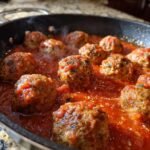 Close-up of several Irresistible Italian Meatballs simmering in a rich, homemade marinara sauce in a black skillet.