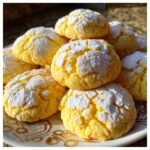 Close-up of bright yellow, powdered sugar-dusted Irresistible Lemon Crinkle Cookies stacked on a decorative white plate.
