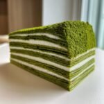 A perfect slice of Irresistible Matcha Mille Crepe Cake showing many thin green layers separated by white cream.