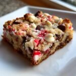 A close-up of an Irresistible Mm Christmas Cookie Bars square topped with white chocolate chips and crushed candy canes.