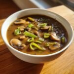 Close-up of Irresistible Mushroom Leek Gravy With Shallots Recipe, featuring sliced mushrooms and bright green leeks in a rich brown sauce.
