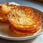 Close-up of a stack of golden brown, lacy Irresistible Parmesan Crisps resting on a light plate.