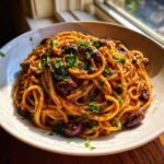 A close-up of a hearty serving of Irresistible Pasta Puttanesca, tossed in a rich sauce with whole olives and fresh parsley.