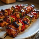 Close-up of three grilled Irresistible Peanut Chicken Kabobs glistening with sauce, alternating with colorful peppers and onions.