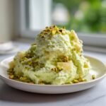 A generous serving of light green, fluffy dessert topped with chopped pistachios and pineapple chunks, showcasing the Irresistible Pistachio Pineapple Fluff Recipe.