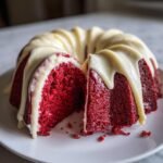A slice cut from an Irresistible Red Velvet Bundt Cake, topped with thick white cream cheese glaze.