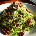 A vibrant mound of Irresistible Shaved Brussels Sprouts Salad Recipe Delight topped with pecans, dried cranberries, and grated cheese.