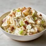 A creamy, chunky bowl of Irresistible Snickers Salad featuring apples, caramel, and a creamy dressing, topped with crumbs.