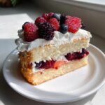 A slice of Irresistible Sparkling Berry Champagne Cake topped with whipped cream and mixed fresh berries.
