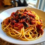 A close-up of a white bowl filled with spaghetti topped generously with a rich, chunky, Irresistible Spicy Eggplant Pasta sauce.