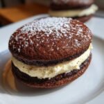 A close-up of one of the Irresistible Tiramisu Cookies, featuring two dark chocolate cookies sandwiching a thick layer of cream filling and dusted with powdered sugar.
