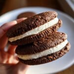 Two Perfectly Spiced Gingerbread Sandwich Cookies stacked, showing rich dark cookies and thick cream filling.
