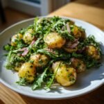 A close-up of Refreshing Arugula Potato Salad featuring small yellow potatoes, bright green arugula, and slivers of red onion.