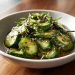 Close-up of sliced cucumbers coated in a savory Asian dressing, topped with sesame seeds and herbs for a Refreshing Easy Asian Cucumber Salad.