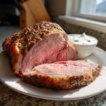 A thick slice of medium-rare Savory Prime Rib Roast with a seasoned crust, served next to horseradish sauce.