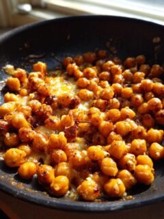 Close-up of Irresistible Skillet Cheesy Chickpeas browning and melting cheese in a black frying pan.